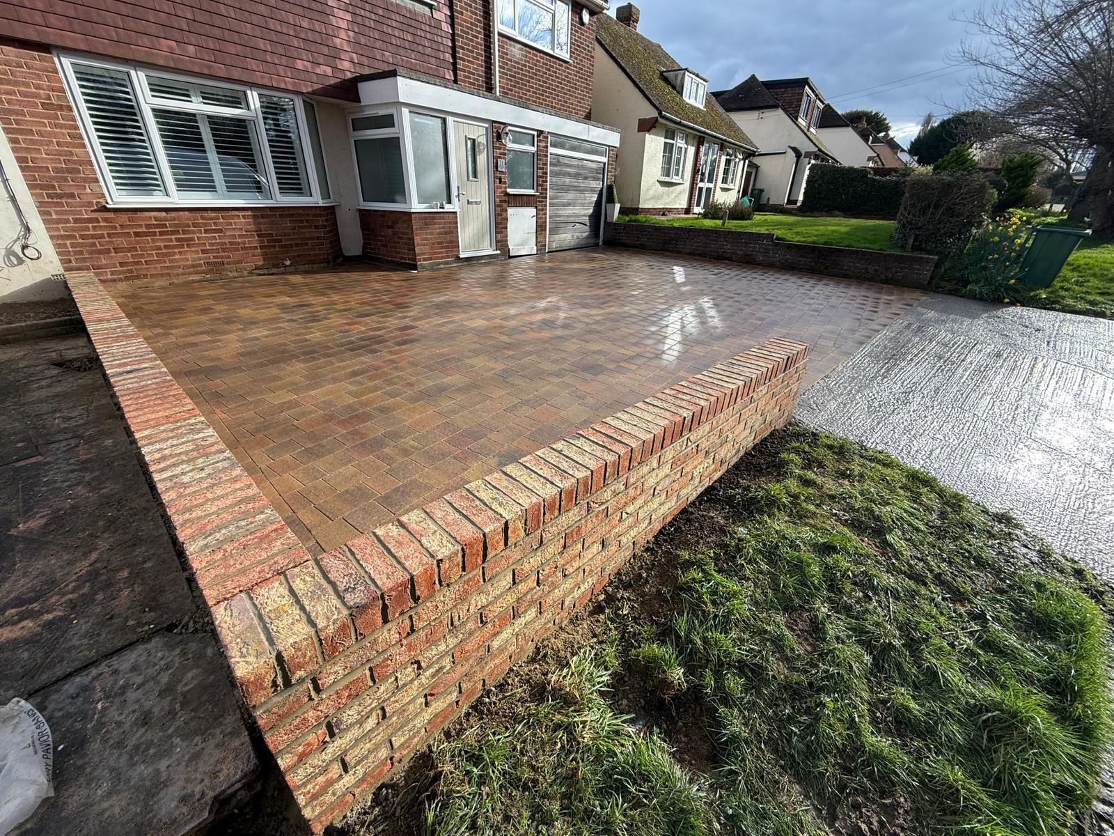 Finished brindle block paving driveway with a brick dwarf wall beside the lawn