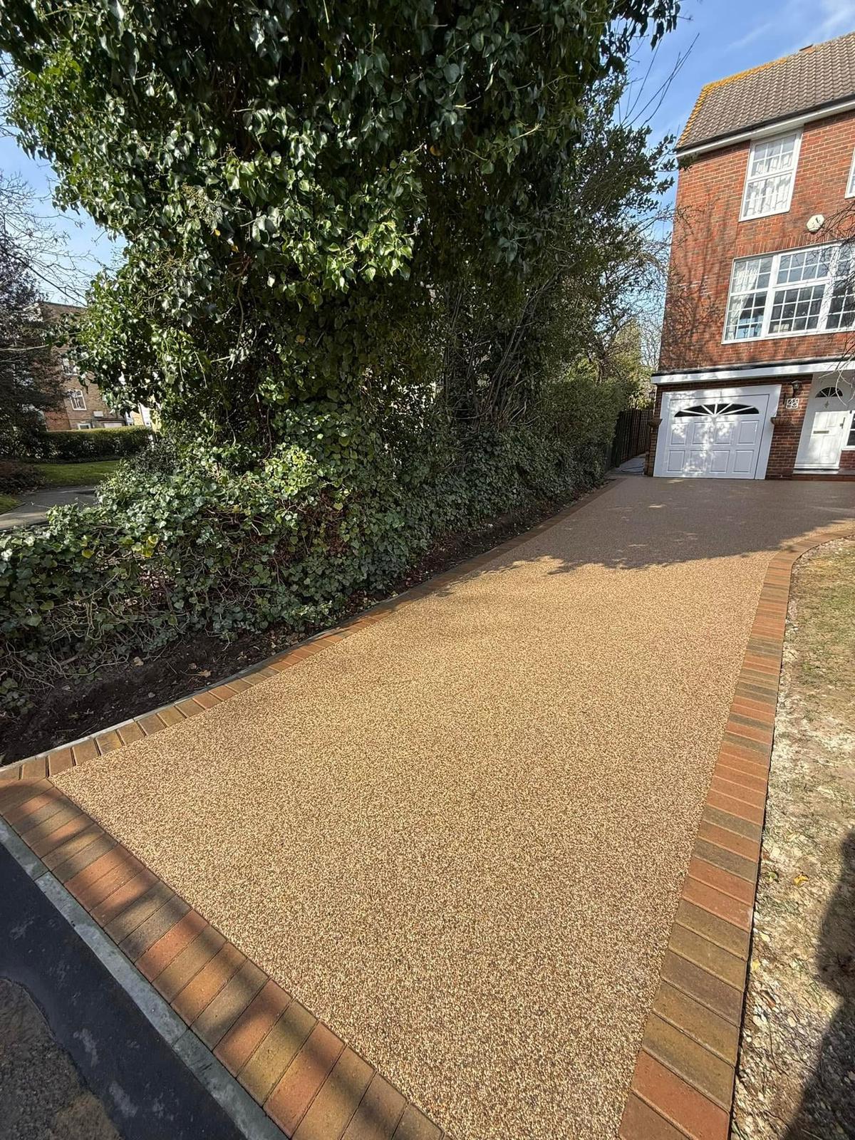 New golden resin driveway with block paving edging leading to the same white garage